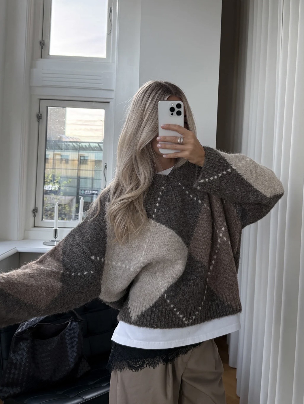 Junge Frau sitzt auf grauem Sofa, trägt gemusterten Pullover und Brille, lehnt entspannt im Studio.